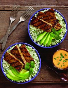 two bowls filled with rice, meat and veggies on top of a wooden table