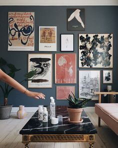 a living room filled with lots of pictures and plants on the wall next to a coffee table