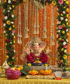 there is an elephant statue in front of flowers and garlands on the wall with bells hanging from it