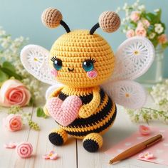 a crocheted bee sitting on top of a table next to flowers and a pen