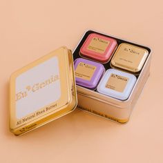 four small square tins with the word butter genius in them on a pink background