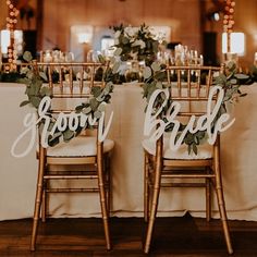 two wooden chairs sitting next to each other on top of a table covered in greenery