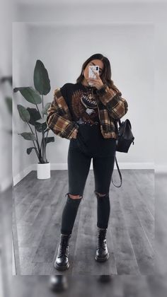 a woman taking a selfie while wearing black ripped jeans and a plaid shirt with an animal print on it