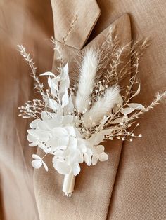 a boutonniere with white flowers and feathers on the lapel of a suit