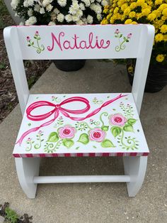 a white wooden chair with pink and green designs on it, sitting in front of flowers