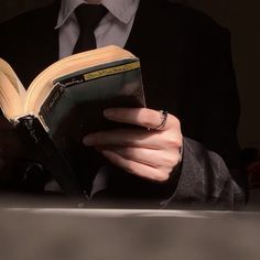 a person wearing a suit and tie reading a book with their hands on the pages