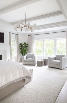 a bedroom with white walls and carpeted flooring, two armchairs in front of the bed