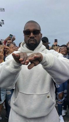 a man in a white hoodie is holding his hands out to the camera while people take pictures