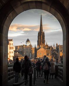 a group of people walking across a bridge over looking a city with tall buildings in the background