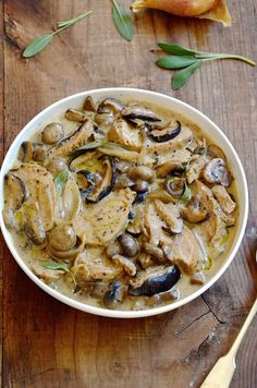 a bowl filled with meat and mushrooms on top of a wooden table next to garlic