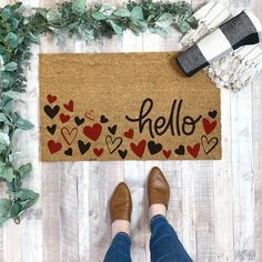 a person standing in front of a door mat that says hello with hearts on it