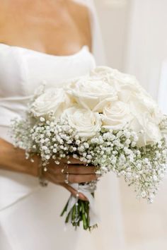 a bride holding a bouquet of white roses and baby's breath in her hand