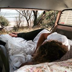 a person laying in the back of a car on top of a bed next to trees