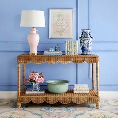 a wicker shelf with vases and books on it in front of a blue wall