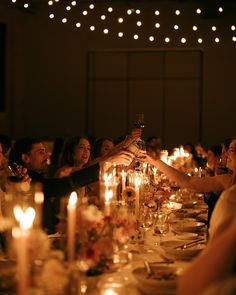 a group of people sitting around a dinner table toasting with wine glasses in front of them