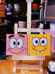 two square paintings with faces on them sitting on a wooden easel