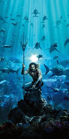 a man holding a spear standing on top of a rock in front of an aquarium filled with fish