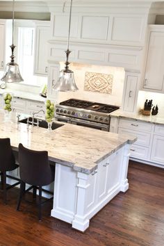 a large kitchen with an island in the middle and chairs at the counter top, along with two pendant lights hanging from the ceiling