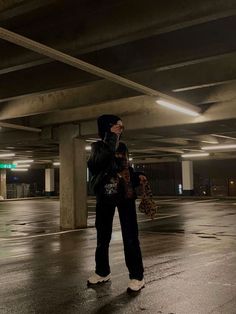 a man standing in an empty parking garage talking on his cell phone while holding a purse