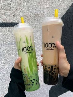 two people holding up drinks in front of a white wall with the words 100 % written on it