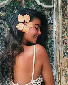 a woman with a flower in her hair standing next to a wooden wall and smiling