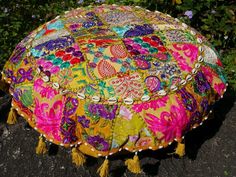 a colorfully decorated round pillow sitting on top of a stone slab in front of some flowers