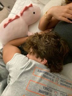 a young man laying on top of a bed next to a stuffed animal pig toy