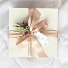 a wedding card with a pink flower and ribbon tied around it on top of a white sheet