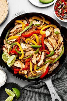 a skillet filled with chicken, peppers, and avocado on top of a table