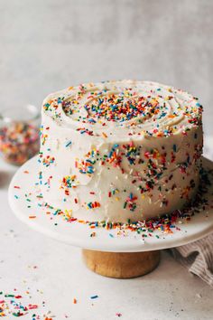 a cake with white frosting and sprinkles sitting on a wooden stand