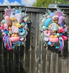 two wreaths with stuffed animals hanging from them on a wooden fence next to each other