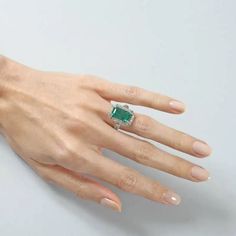 a woman's hand wearing a ring with an emerald and diamond center on it