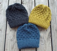 three knitted beanies sitting on top of a wooden floor next to each other