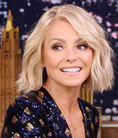 a woman with blonde hair and blue eyes smiles at the camera in front of a big ben clock tower