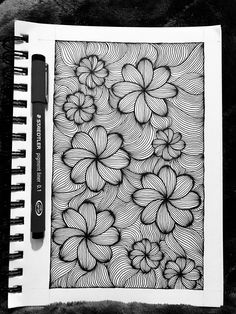 a black and white drawing of flowers on a piece of paper next to a pen