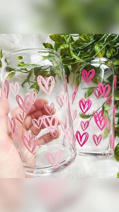 two clear vases filled with pink hearts on top of a white table next to greenery