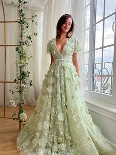 a woman standing in front of a window wearing a green dress with flowers on it