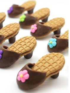 chocolate covered shoes with flowers on them sitting on a white table next to other cookies