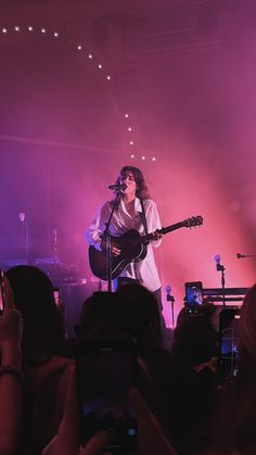 a woman singing into a microphone while holding a guitar in front of an audience at a concert