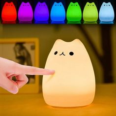 a person pointing at a cat shaped light on a table with other cats in the background