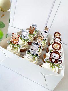 cupcakes decorated with monkey and giraffe toppers in a white box