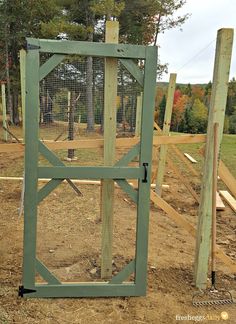 an open gate in the middle of a dirt field with trees and grass behind it