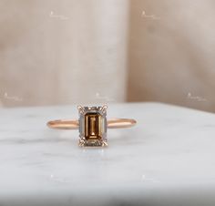 a ring with an emerald colored stone on it sitting on a marble table next to a white wall