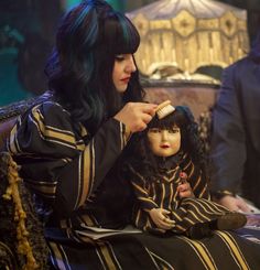 a woman with long black hair sitting next to a doll