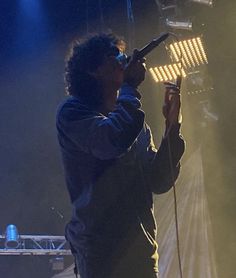 a man holding a microphone up to his mouth while standing in front of a stage