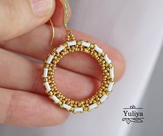 a hand holding a gold and white beaded hoop earrings