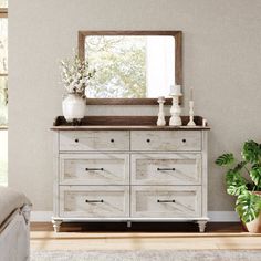 a white dresser sitting in front of a mirror next to a bed and potted plant