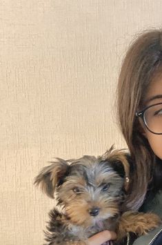 a woman holding a small dog in her arms and smiling at the camera while wearing glasses