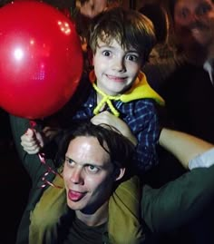 a man holding a red balloon while standing next to a young boy