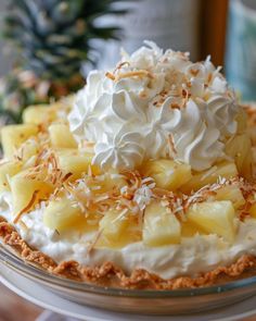 a pie with whipped cream, pineapple and coconut on top sitting on a table